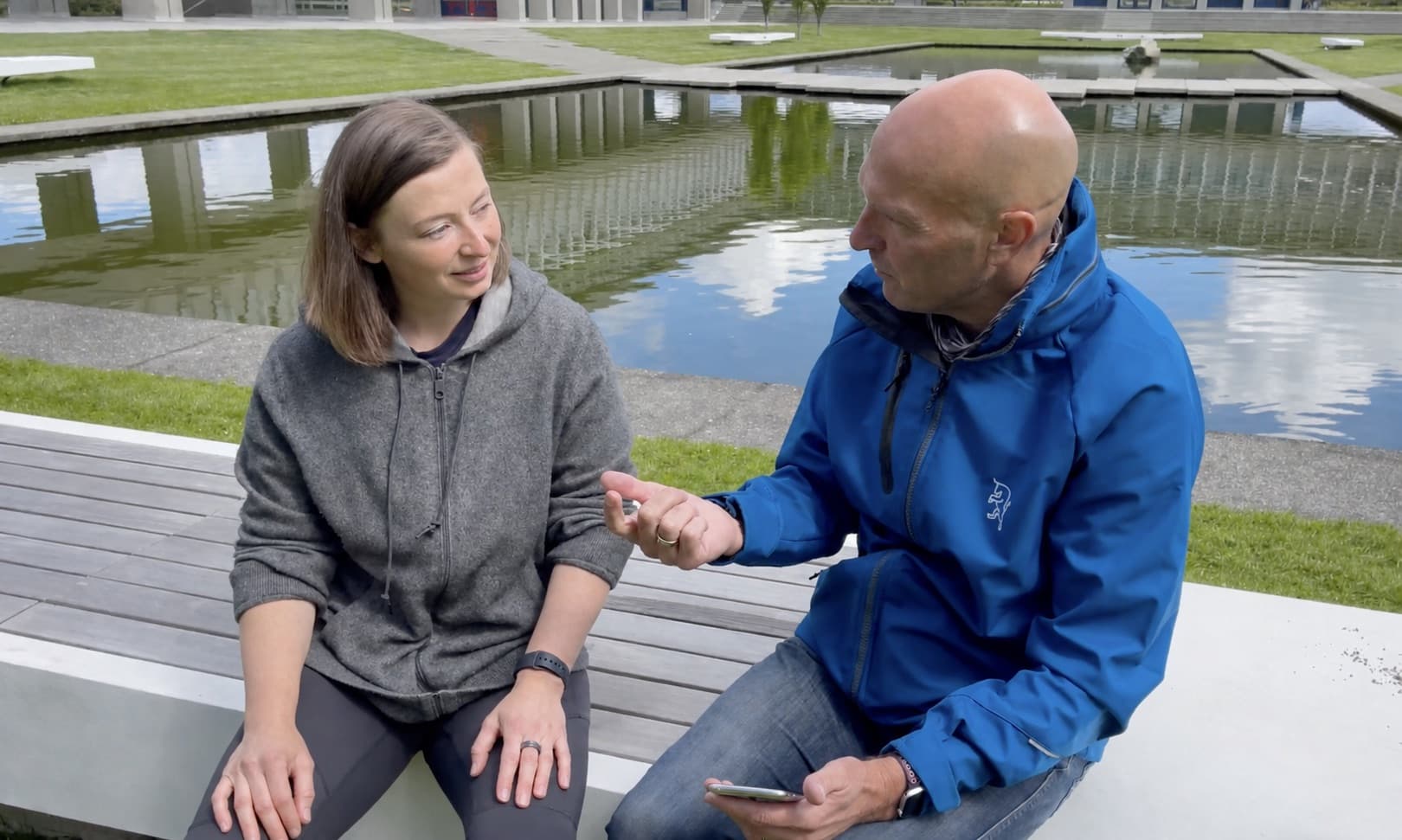 A Pieoneers representative speaking with Jerry Kroll beside a reflecting pool in Vancouver.